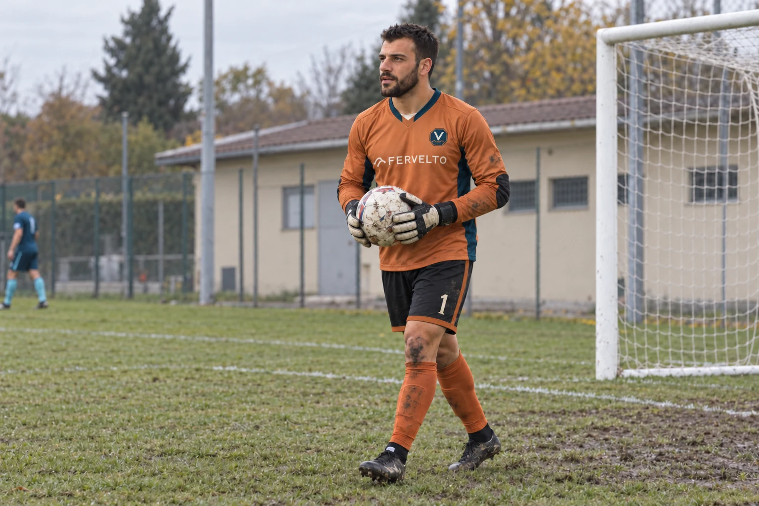 Matteo Barzani in divisa arancio a maniche lunghe cammina con il pallone fra i guanti davanti alla porta, su erba umida.